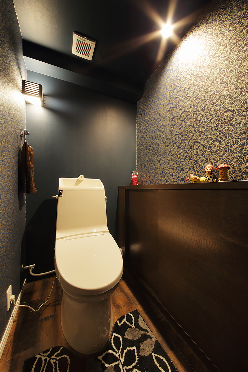 トイレはぐっとシックに落ち着いたモダンスタイル。引き締め色の壁とアラベスクタイルを思わせるクロス、そして間接照明が高級感を醸し出す。