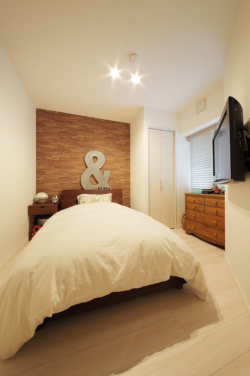寝室はコンパクトながらも収納を備えて使い勝手よいスペースに。木目調のデザインウォールで落ち着いた高級感を出している。