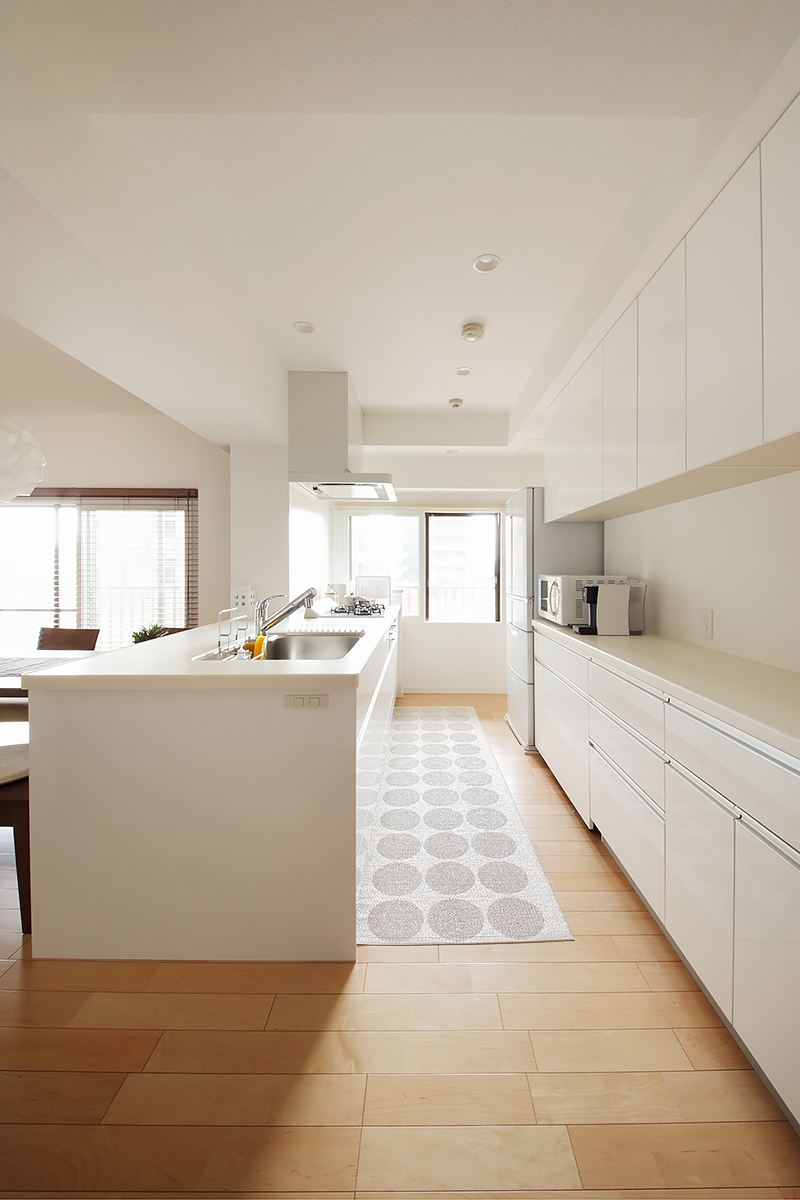 白で統一されたキッチンは収納も大容量。奥の右手からは本棚コーナーや玄関に通じる収納スペースへと繋がり、回遊式になっている。