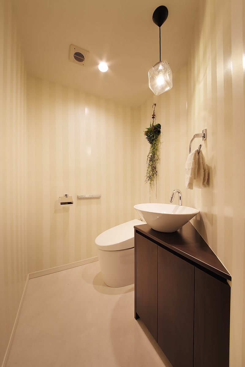 広くゆったりとしたトイレは、ストライプのクロスやレトロな照明と手洗いボウルでお洒落な空間に。隅々にまで奥様のセンスが生かされている。