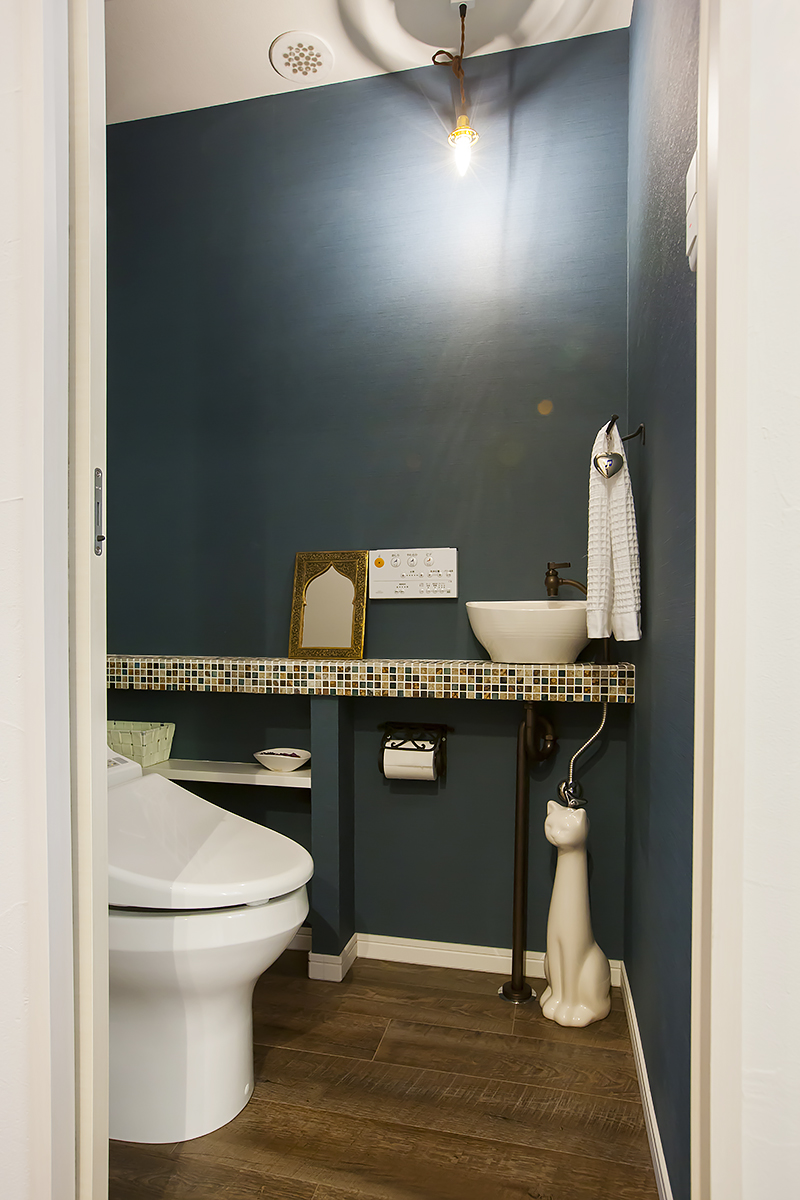 深いブルー系の壁が落ち着いた印象のトイレ。手粗利ボウルを設置したタイル貼りの台がいい味を出している。